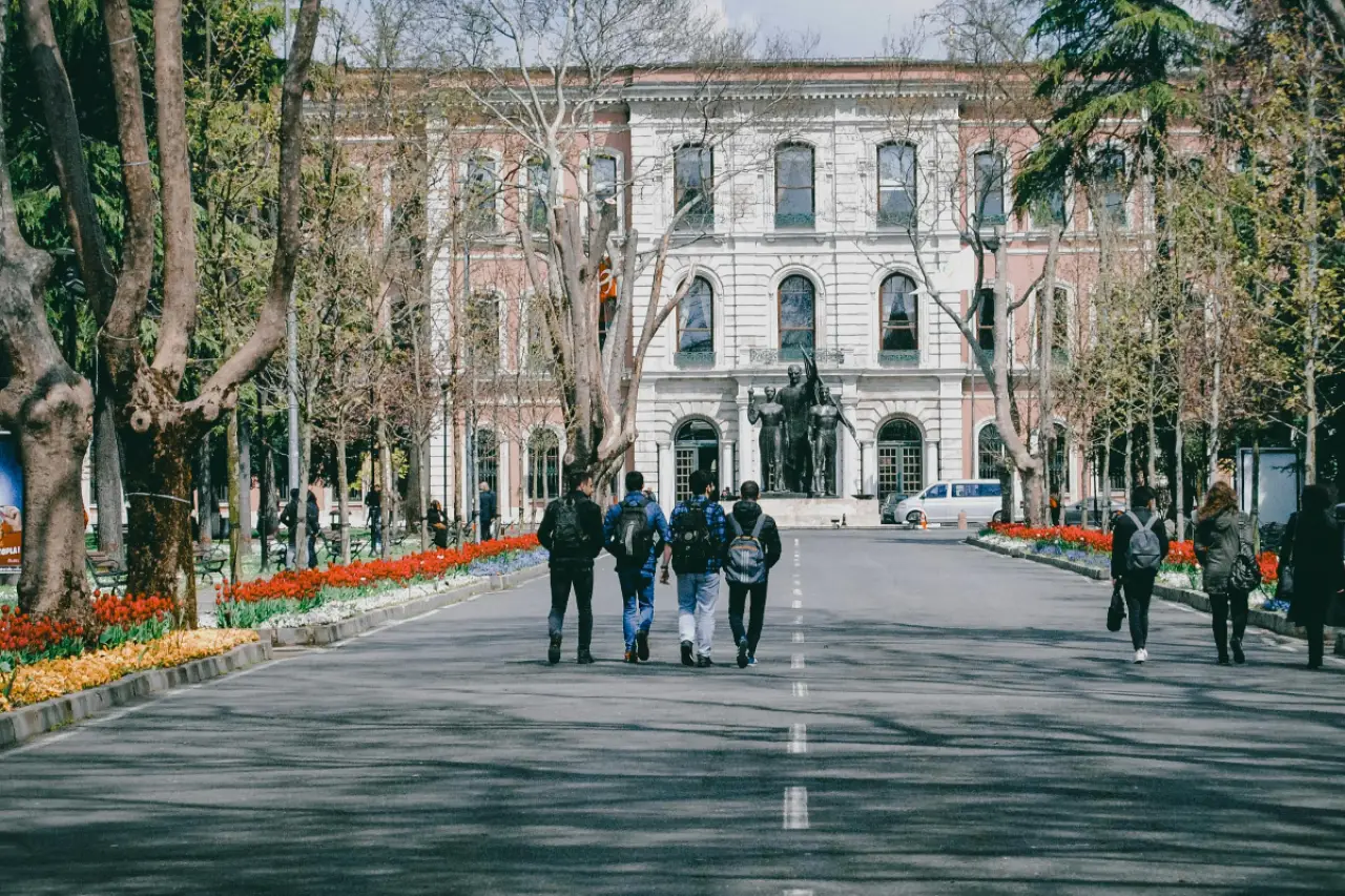 Üniversite binası önünde, dört sırt çantalı genç öğrenciler