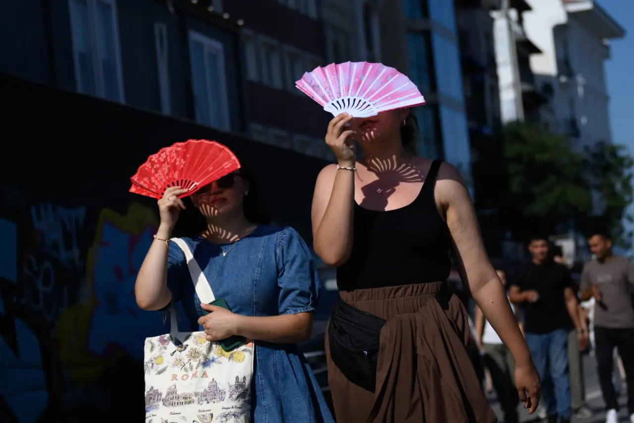 İstanbul'da yaz ayında sıcak hava, açık alanda iki kadın ellerinde kırmızı ve pembe yelpazelerle yüzlerini gölgelemek için yelpazeleri kullanırken yürürken