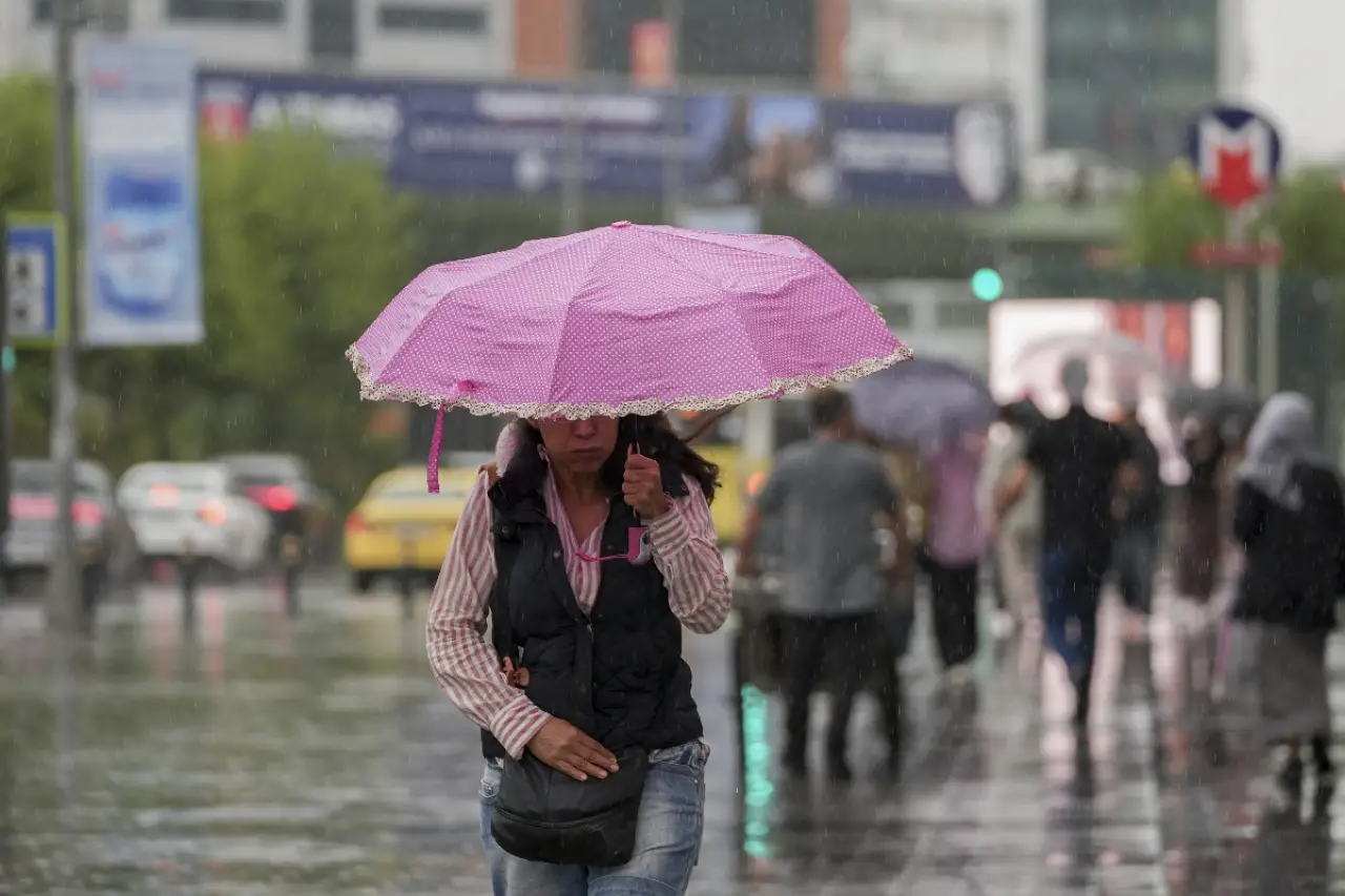 İstanbul'da yağmur altında pembe bir şemsiyeyi tutan bir kadın, kalabalık bir sokakta yürümektedir. Arkada birkaç kişi de şemsiye ile yürürken, sokak yağmur suyu ile dolmuş durumdadır. Şehir manzarası ve sarı taksiler görünmektedir.