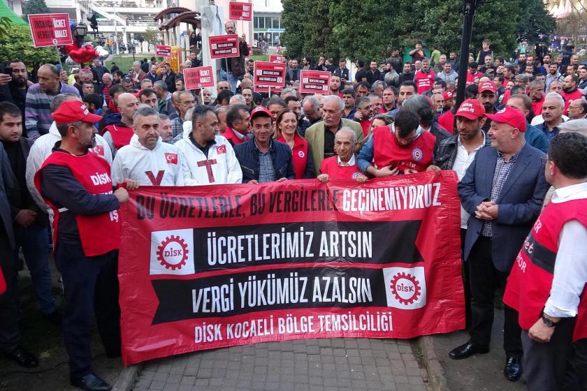 DİSK üyeleri, 'Bu ücretlerle, bu vergilerle geçinemiyoruz', 'Ücretlerimiz artsın, vergi yükümüz azalsın' yazılı pankartın arkasında basın açıklaması gerçekleştirirken