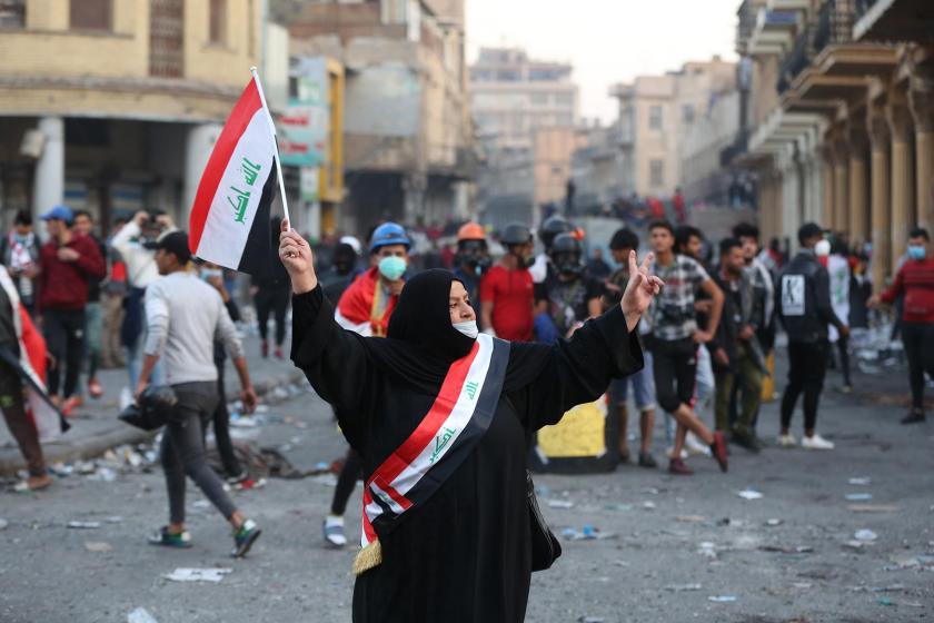 Woman protester holding a flag at her hand, in front of the crowd in Iraq. 