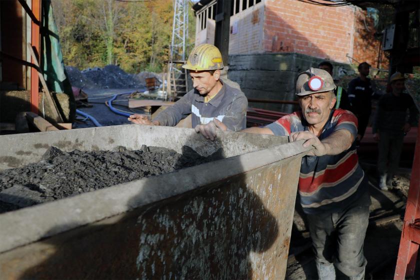 Yer üstünde kömür kovasını iten maden işçileri