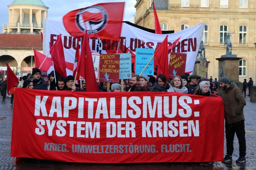 Almanya Stuttgart'ta mülteci haklarının korunması için yapılan eylemde 'Kapitalizm: Kriz sistemi' yazılı pankart ve arkasında duranlar