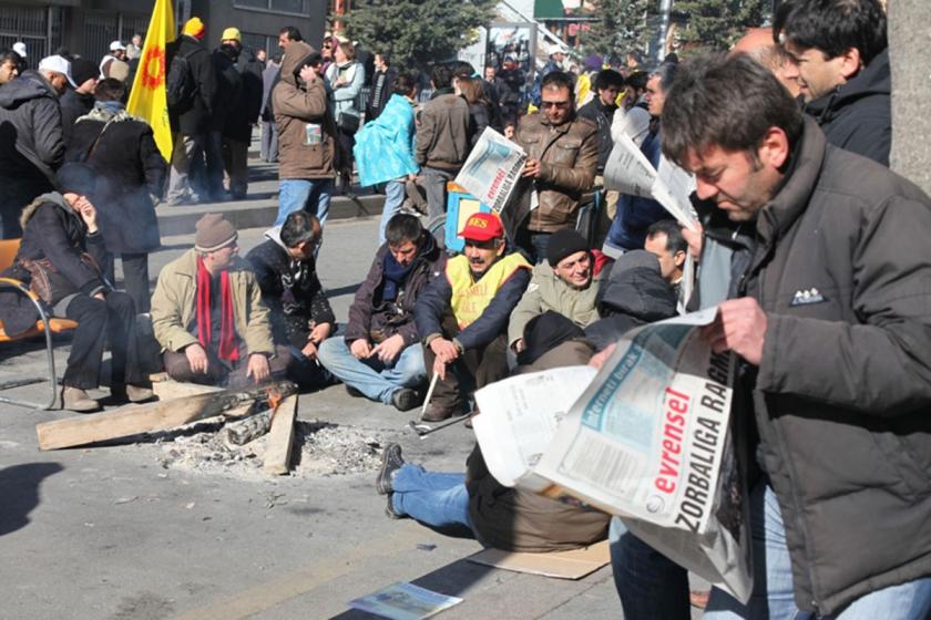 Bir işçi-emekçi eyleminde ateş başında oturmuş emekçilerin bazıları Evrensel okuyor.