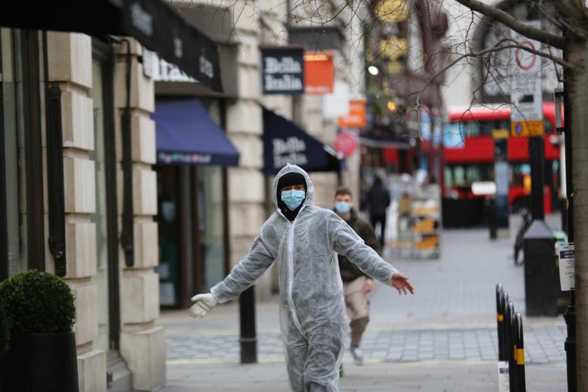 İngiltere'de koronavirüs (Kovid-19) salgını yüzünden boş caddede koruyucu giysi ve maske ile dolaşan bir erkek.