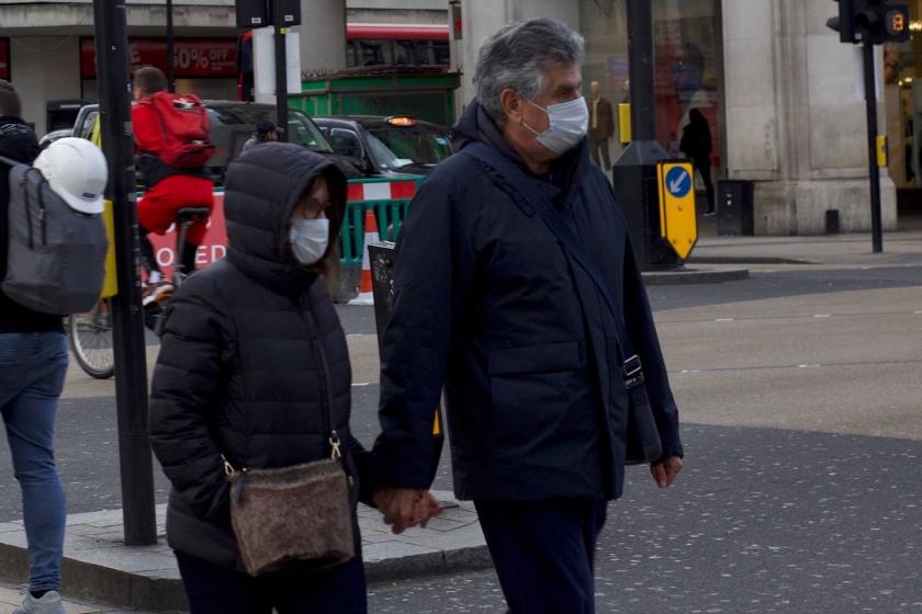 İngiltere'de koronavirüs (Kovid-19) salgını yüzünden yüzlerinden maske ile dolaşan ve el ele tutuşmuş bir erkek ve bir kadın.