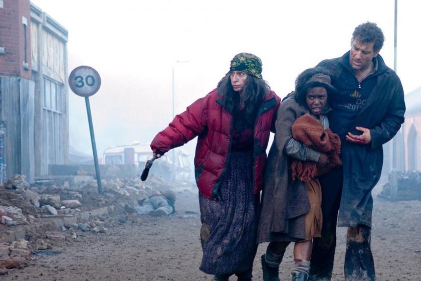 Children of Men filminden bir kare, yıkık dökük bir sokak, bir kadın etrafa bakıyor, yanında bir kız çocuğu ve erkek