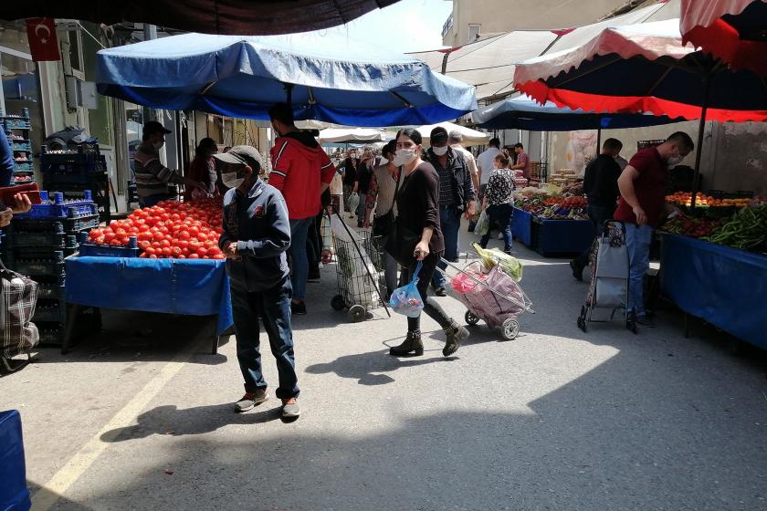 Semt pazarında alışveriş yapmaya çalışanlar, solda eli boş bir erkek, ortada elinde pazar arabası olan kadın, sağda sebze seçen erkek