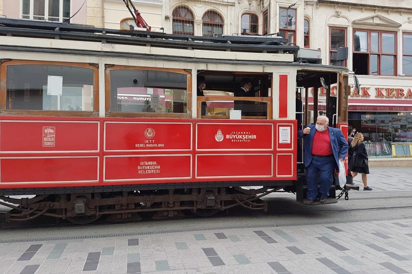 Yüzünde cerrahi maske olan bir erkek, İstiklal Caddesi üzerinde sefer yapan nostaljik tramvaydan inerken.