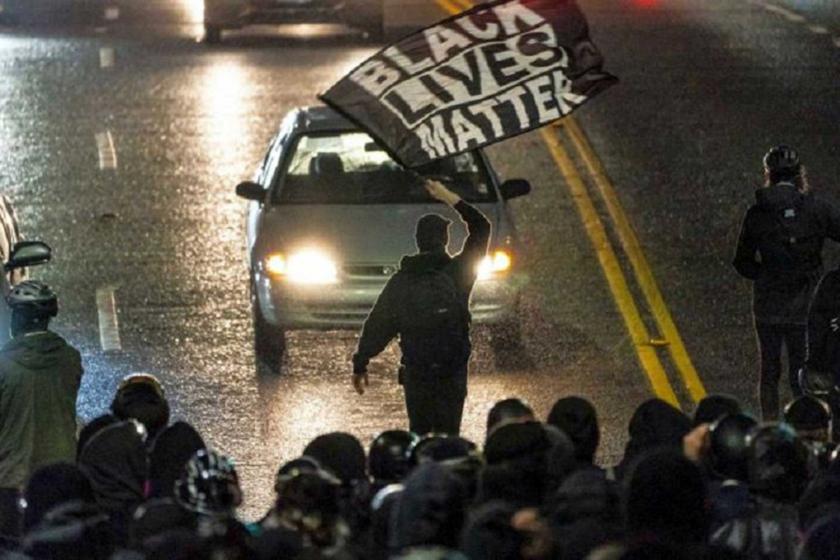 Black lives matter bayrağı taşıyan bir genç arabanın üstüne yürüyor