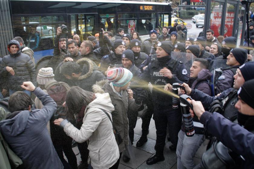 Çok sayıda polis bir grup kişinin yüzüne yakın mesafeden biber gazı sıkıyor.