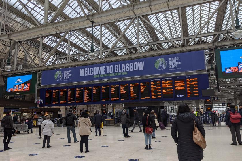 Gara asılmış Glasgow'a hoş geldiniz afişi altında sıra bekleyen insanlar