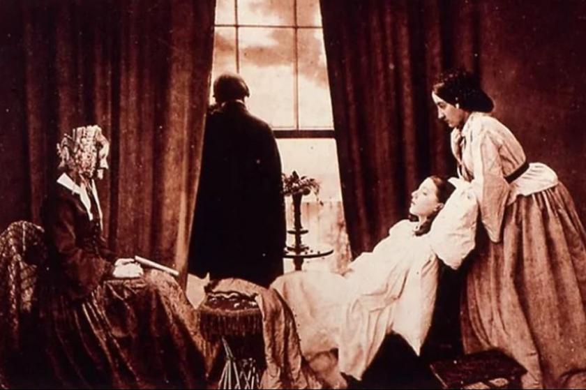 Hasta bir kadının başında bekleyen iki kadın ve camdan dışarıya bakan bir erkek.