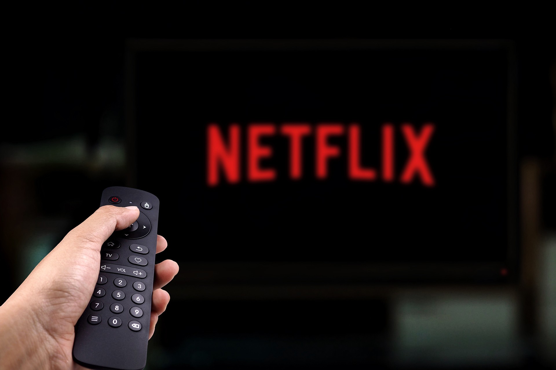 Televizyon ekranında Netflix görüntüsü ve kumanda tutan bir el. 