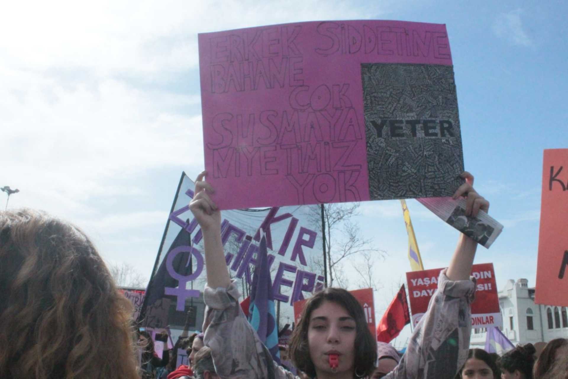 Bir kadın eyleminde elinde 'Erkek şiddetine bahane çok, susmaya niyetimiz yok, yeter' yazılı döviz tutan genç bir kadın.