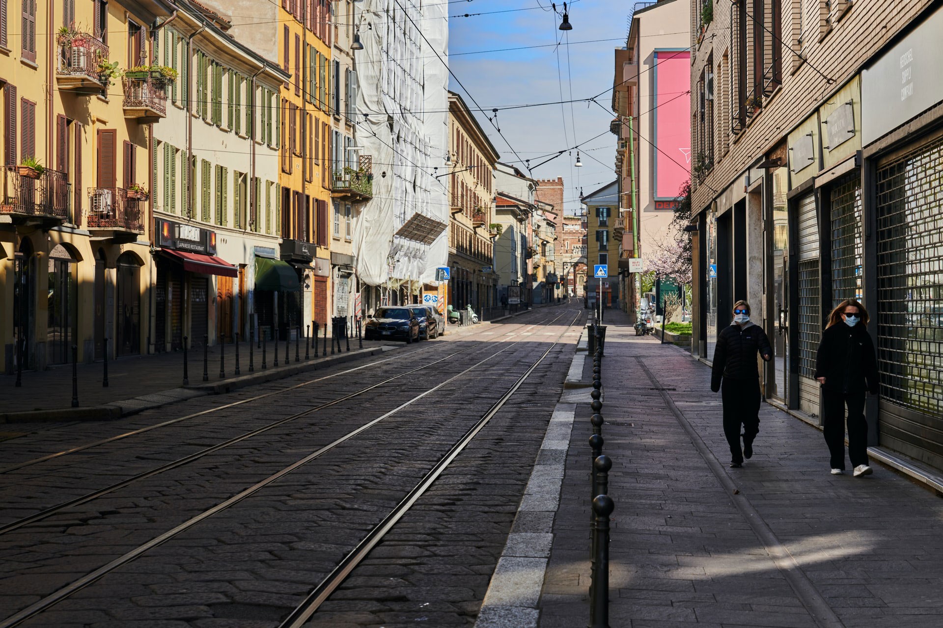 Milano'da sokakta yürüyen yüzü maskeli iki kişi, solda tramvay yolu