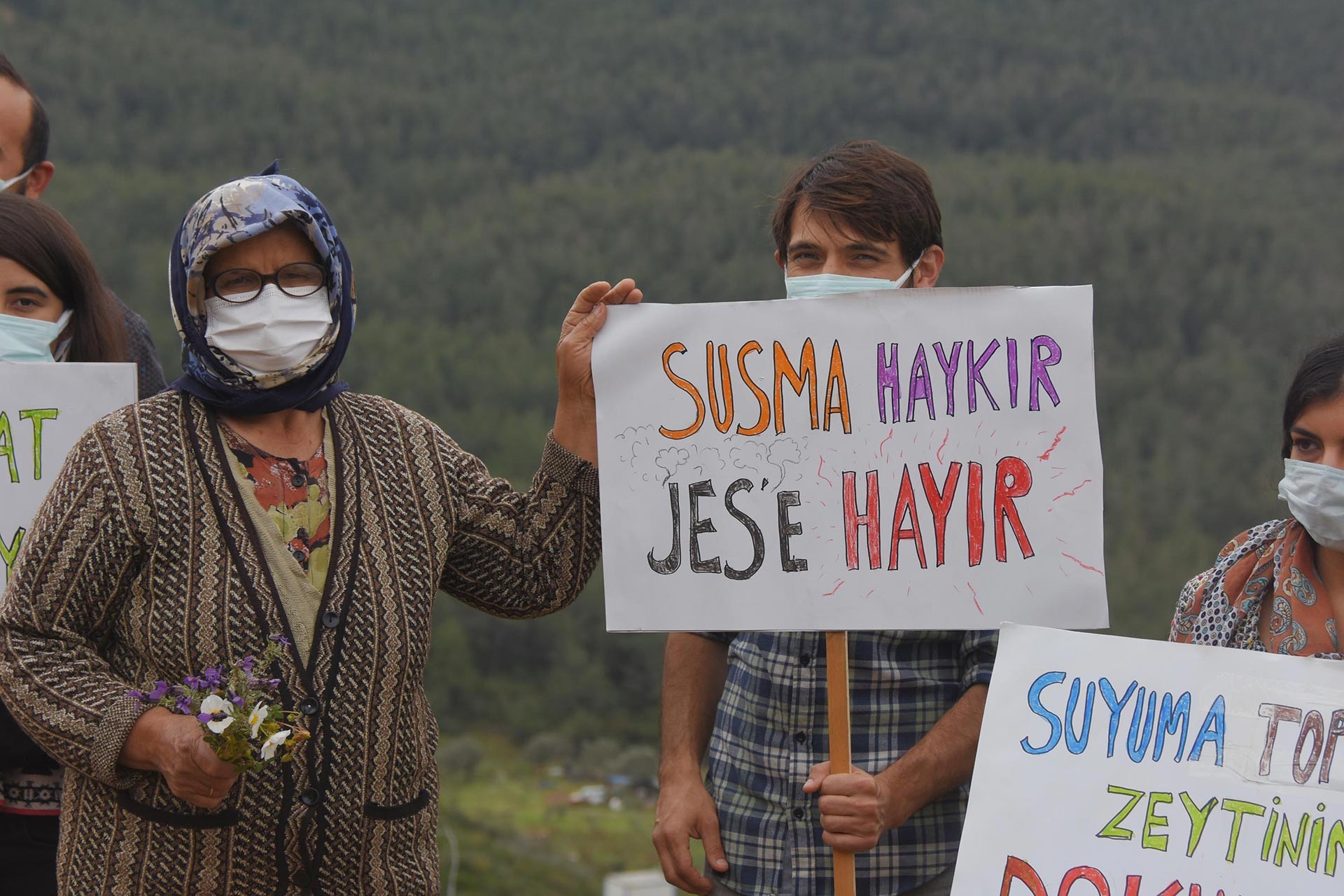 Seferihisar'da JES'e karşı eylem yapan köylüler, solda gözlüklü bir teyze, sağda susma haykır JES'e hayır dövizi