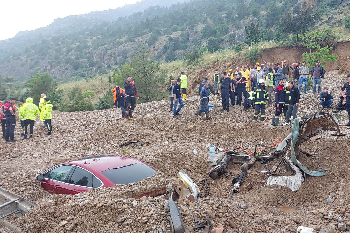 heyelanda toprak altında kalan kırmızı renkli araba ve etrafında görevlilerle birlikte insanlar 